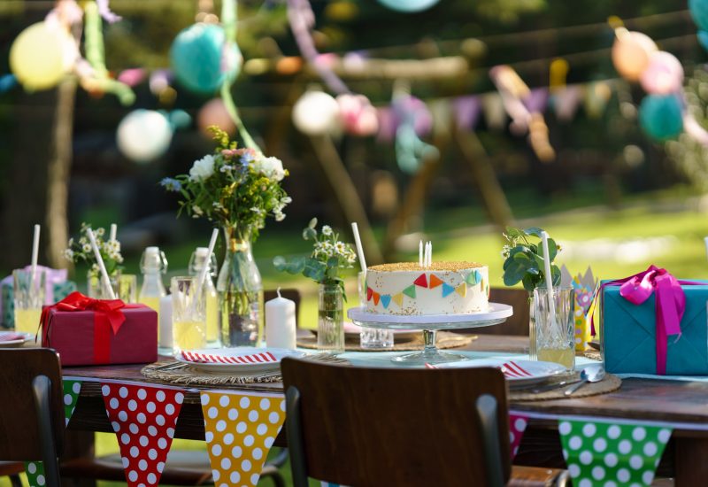 Shot of the birthday table with colorful decorations, birthday cake, and gifts. Inspiration for simple, tasteful birthday decoration for a garden party.